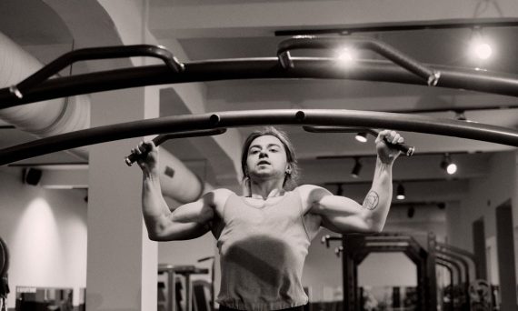 Grayscale image of a man doing pull-ups in a gym, showcasing strength and focus.